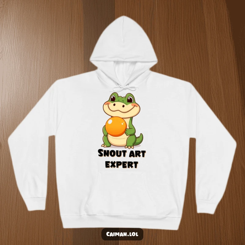 Funny Caiman Hoodie, a warm garment featuring a caiman with a silly expression, balancing a round orange fruit on its snout, showcasing a humorous talent.